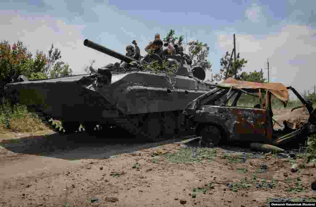 Ukrainian soldiers ride a BMP-1 infantry fighting vehicle near a destroyed car in the village.