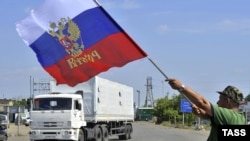 A local resident holds a Russian national flag as trucks, part of a Russian humanitarian convoy, cross the Ukrainian border at the Izvarino custom control checkpoint.