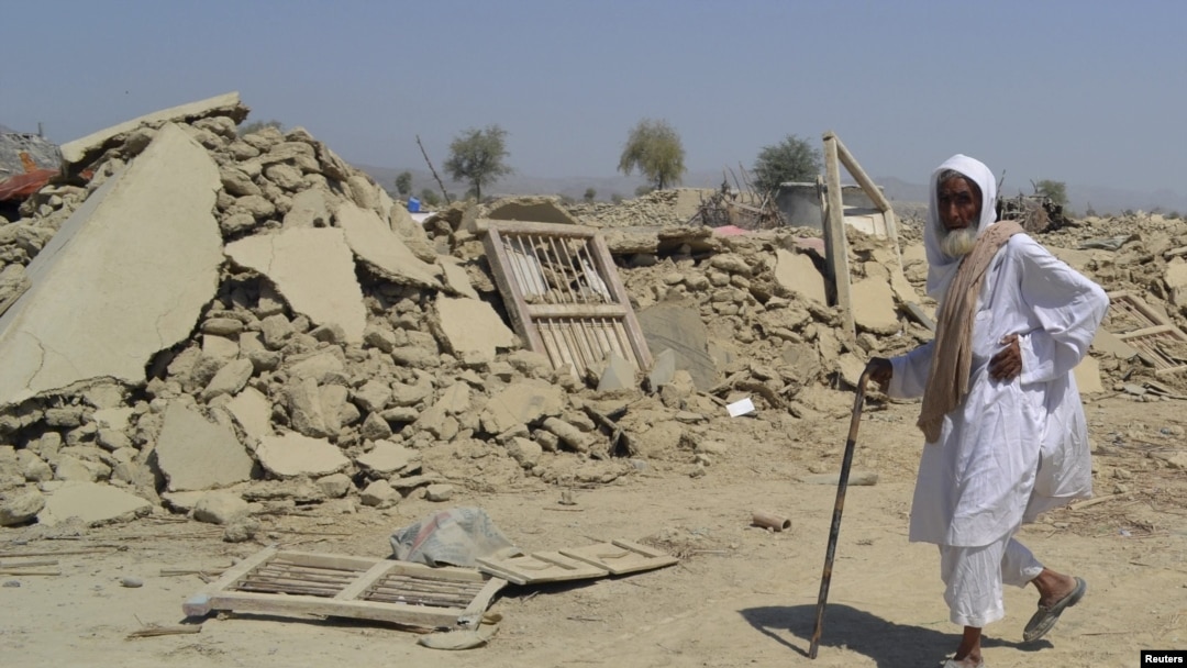 بلوچستان: په اوران کې له زلزلې ورانې شوې یوې کنډواله ودانۍ مخې ته یو سپینږی کس تېرېږي. ۲۵/۰۹/۲۰۱۳ 
