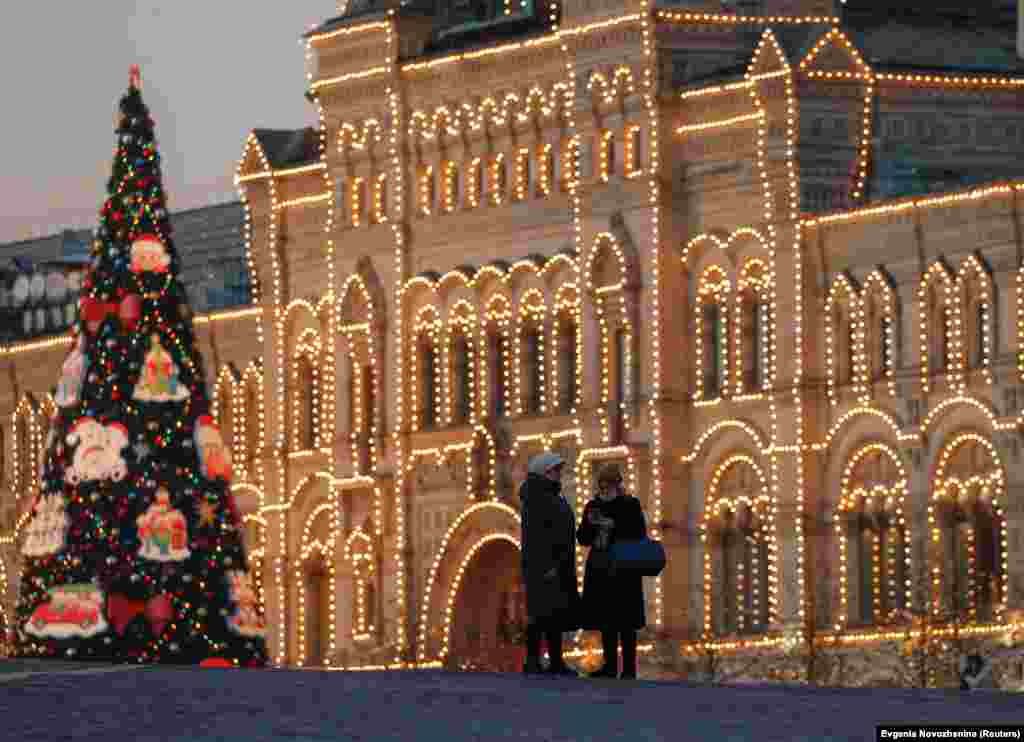 Woman stand beside an ornamented tree in front of Moscow's GUM department store, which is illuminated for the New Year's and Christmas season. Russians routinely refer to decorated seasonal conifers as "New Year firs" or "New Year spruces," a legacy from the Soviet era when religious symbols were frowned upon.