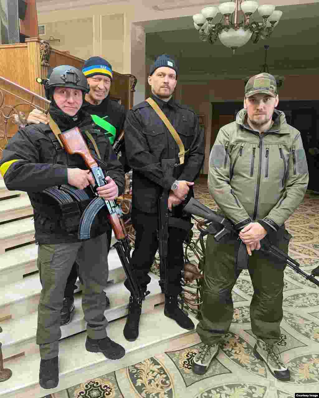 Усик (у центрі праворуч) озброєний власною зброєю в перші дні російського масштабного вторгнення.У лютому 2022 року Усик перебував у Великій Британії, коли дружина надіслала йому смс-повідомлення про те, що Росія здійснила масштабне вторгнення до України. Боксер негайно вилетів до Польщі, потім поїхав до Києва, де вступив до батальйону територіальної оборони