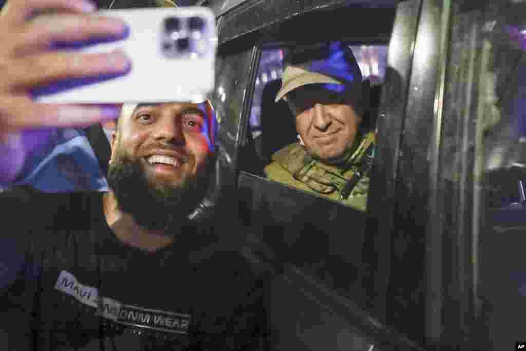 Yevgeny Prigozhin, leader of the Wagner mercenary group, sits inside a military vehicle as a local resident takes a picture with him on a street in Rostov-on-Don, Russia, on June 24. Prigozhin, who sent his fighters to topple the military leaders in Moscow, will leave for Belarus, and a criminal case against him will be dropped as part of a deal to avoid "bloodshed," the Kremlin said on June 24. 