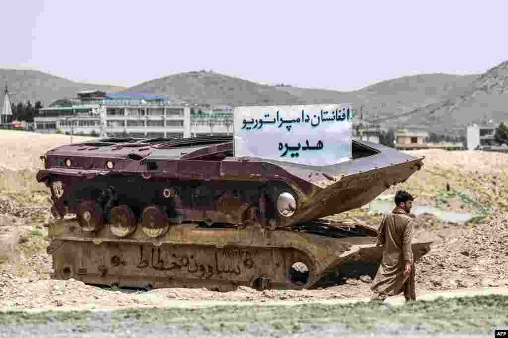 An Afghan man walks past the remains of an abandoned Soviet-era military tank bearing a white board with text in Pashto saying: "Afghanistan: the graveyard of empires."